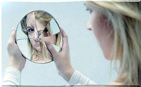 A woman looks at herself in a broken mirror.