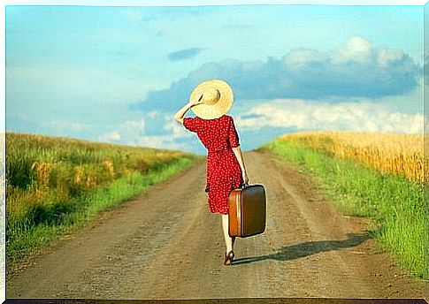 A woman with a suitcase walking on a road.