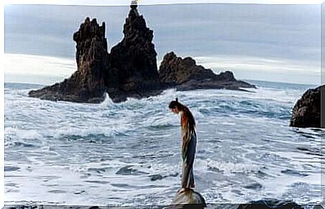 A woman standing on a boulder by the sea